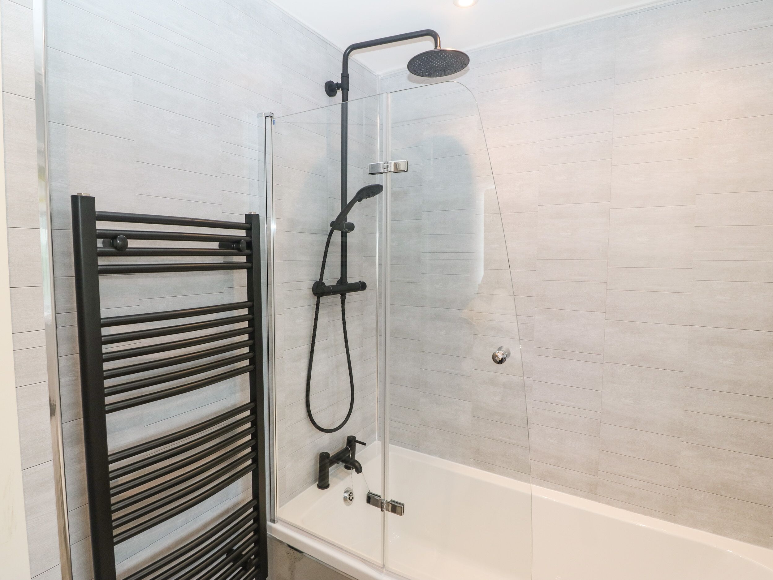 Un box de ducha moderno con puerta de cristal, un perchero negro y un cabezal de ducha manual.