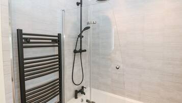 Un box de ducha moderno con puerta de cristal, un perchero negro y un cabezal de ducha manual.