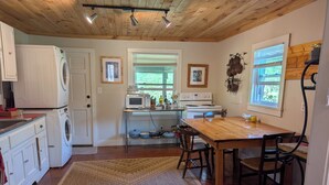 A kitchen with a wooden ceiling, a washing machine, a microwave, a stove, and a dining table with chairs. - Whispering Waters Cabin by The Creek (Fairview)