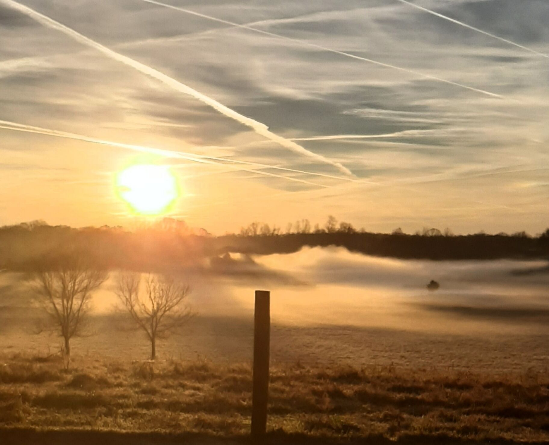 A sunrise over a foggy landscape with a clear sky and a visible contrail.