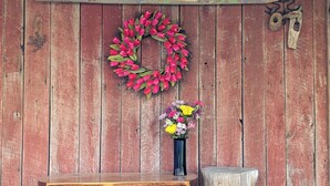 A rustic wooden wall with a 'Earth Home Sweet Home' sign, a red tulip wreath, a vase of colorful flowers, a wooden bench, and a small stool. - Whispering Waters Cabin by The Creek (Fairview)