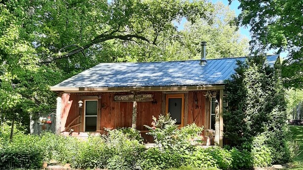A rustic cabin with a metal roof, surrounded by lush greenery and a well-maintained lawn. - Whispering Waters Cabin by The Creek (Fairview)
