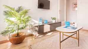 Habitació d'hotel moderna amb una planta gran en test, un televisor de pantalla plana penjat a la paret, un minibar i una taula petita amb una sovina blava.