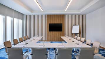 A conference room with a long table, chairs, a projector screen, and a whiteboard.