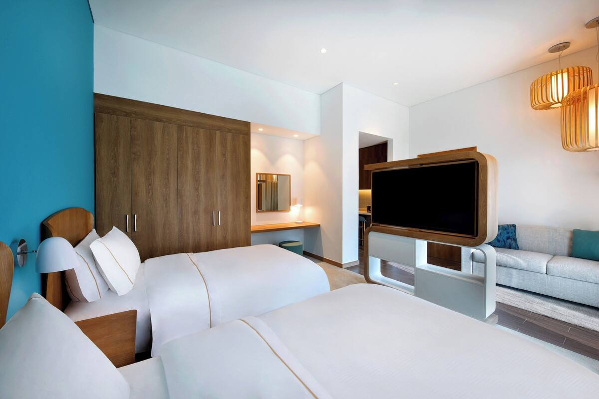A modern hotel room with a large bed, a TV, a sofa, and a wooden wardrobe.