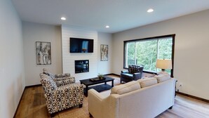 A modern living room with a fireplace, a large window, and a flat-screen TV mounted on the wall. - The Blue Ox on Gull, 5 Bed 5 Bath Resort Home, Sleeps 17 with Boat Slip on Gull Lake (Lake Shore)