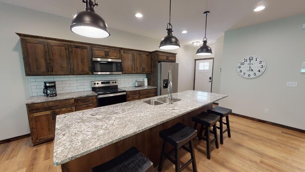 A kitchen with wooden cabinets, a stainless steel microwave, a refrigerator, granite countertops, and bar stools. - The Blue Ox on Gull, 5 Bed 5 Bath Resort Home, Sleeps 17 with Boat Slip on Gull Lake (Lake Shore)