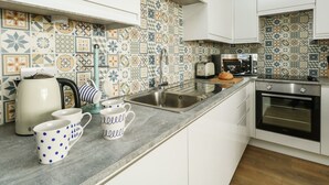 Una cucina con mobili bianchi, zoccolo di piastrelle, lavello, tostapane, bollitore e due tazze a pois.