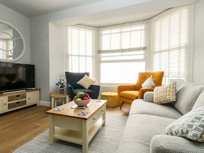 A living room with a TV, two armchairs, a sofa, a coffee table with fruit, and a mirror on the wall. - The Kings Statue (Weymouth)