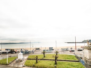 A coastal view with a beach, a statue, and a road leading to a building with a sign. - The Kings Statue (Weymouth)