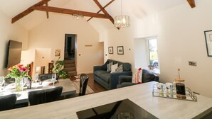 Ein geräumiger Wohnbereich mit hoher Decke und freiliegenden Holzbalken, ein Essbereich mit Tisch für vier Personen und eine gemütliche Sitzecke mit Sofa und Kaffeemaschine.