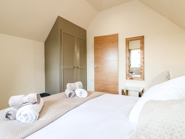 A hotel room with a bed, a wooden wardrobe, a mirror, and towels on the bed.