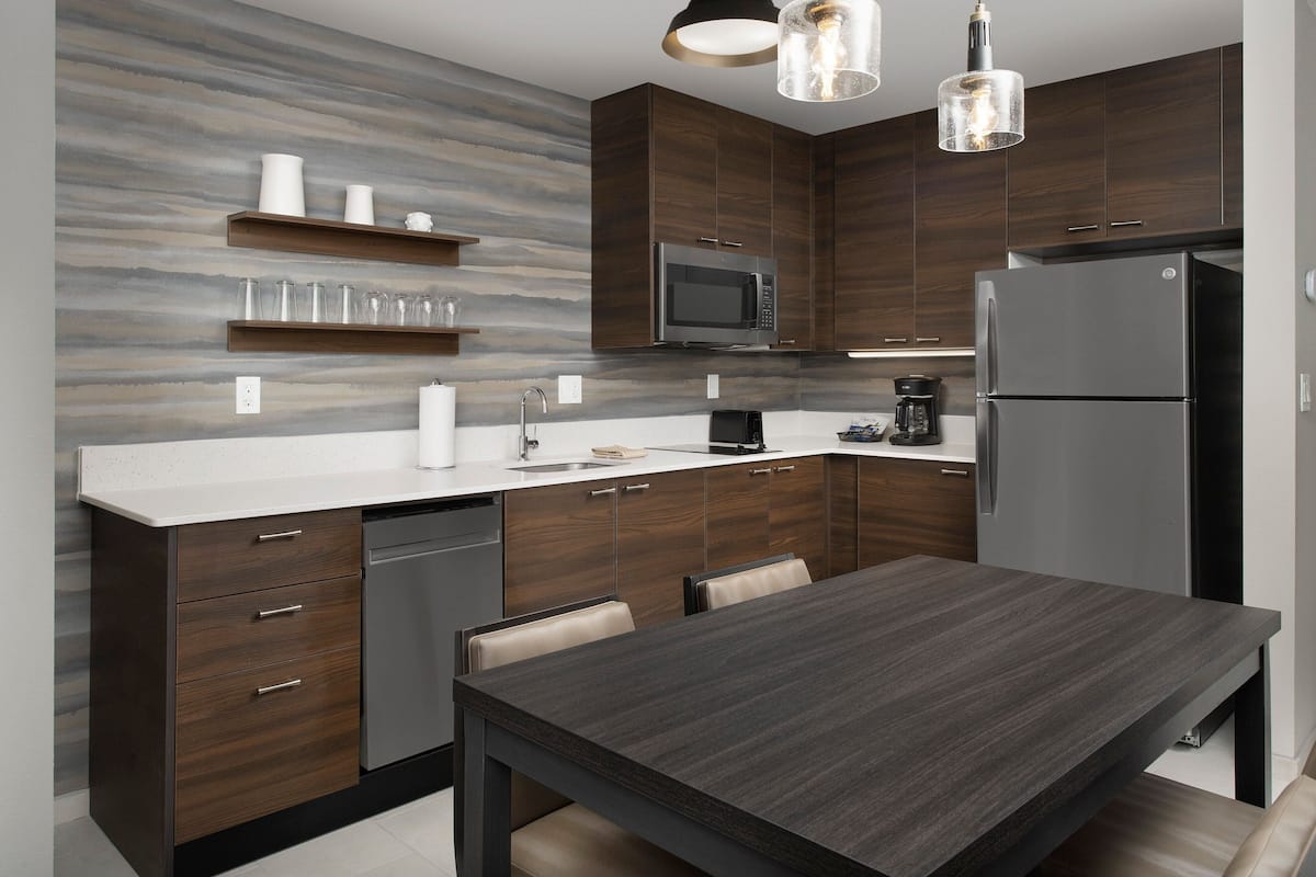 Una cocina moderna con armarios de madera oscura, encimera blanca y electrodomésticos de acero inoxidable.