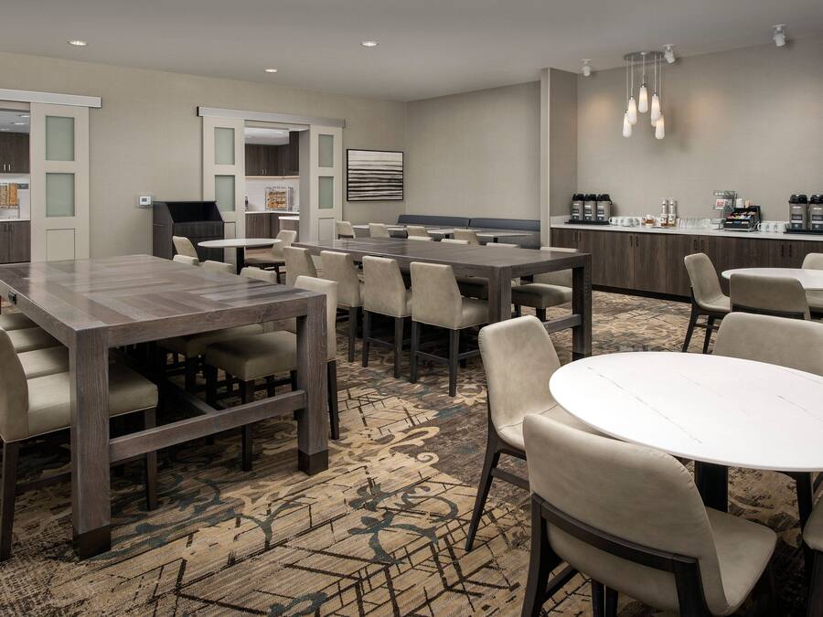Uma sala de jantar de hotel com várias mesas e cadeiras, uma área de cozinha e um espaço para café.