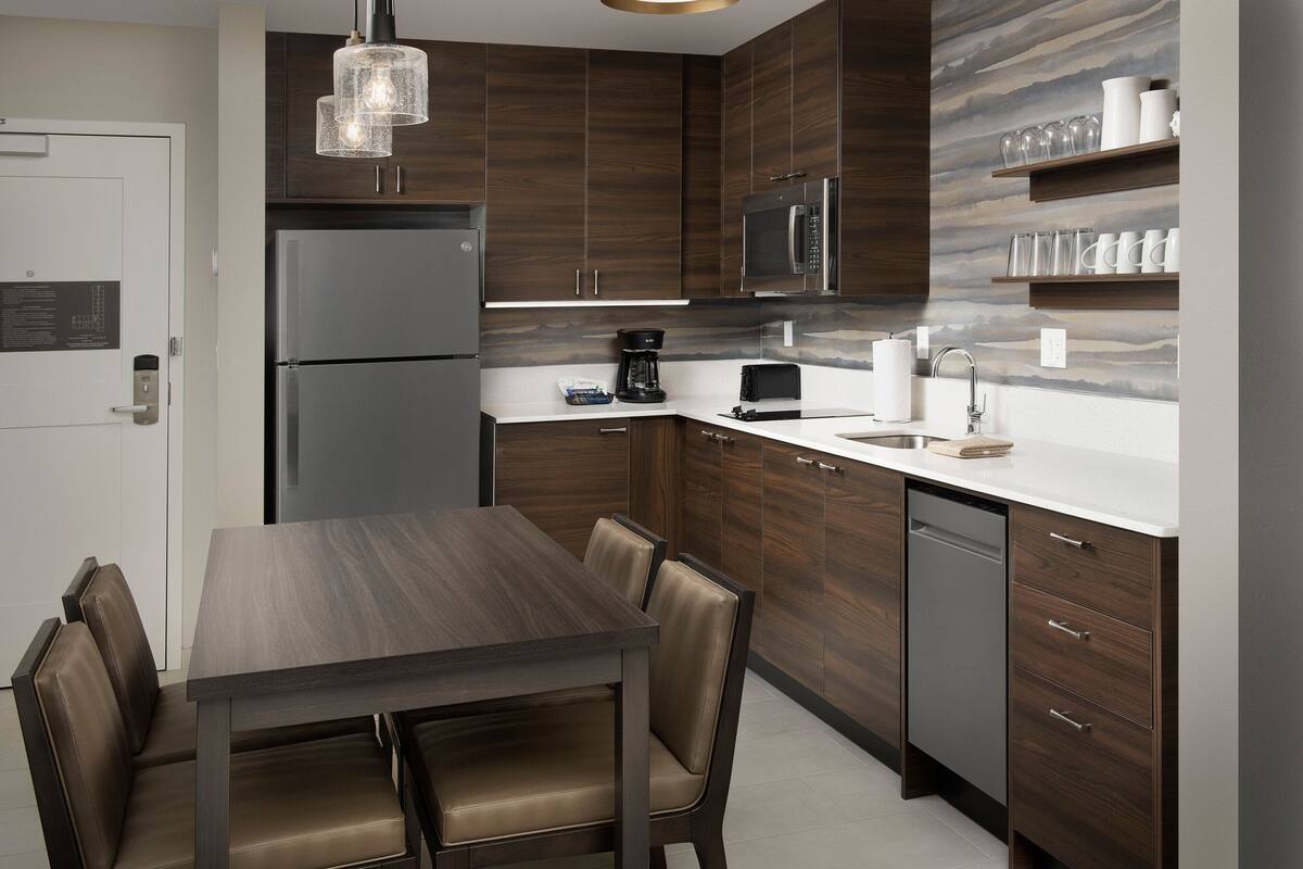 Una cocina moderna con armarios de madera oscura, electrodomésticos de acero inoxidable y un comedor con mesa de madera y sillas de cuero.