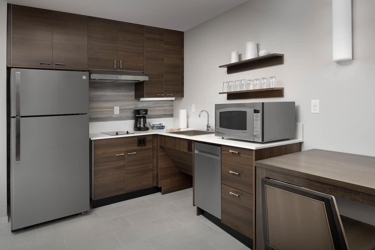 Una cocina moderna con gabinetes de madera oscura, electrodomésticos de acero inoxidable y encimera blanca.