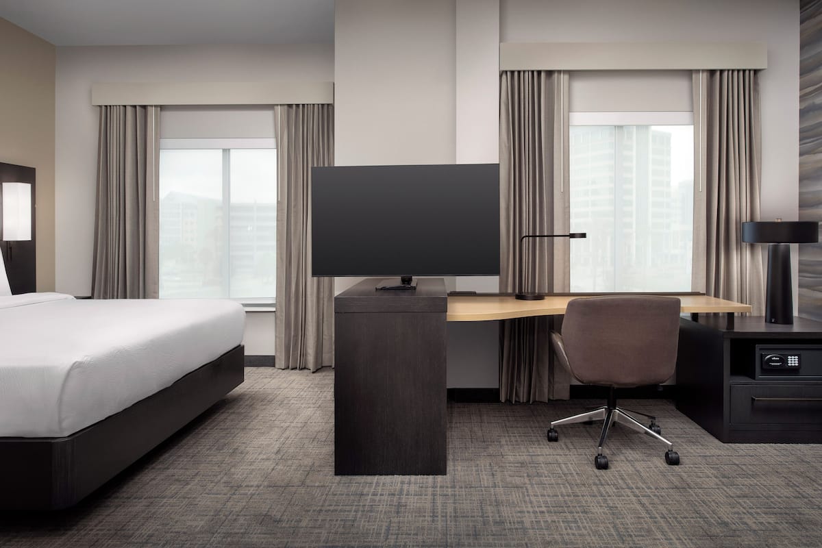 Una habitación de hotel moderna con una cama, un escritorio, una silla, un televisor y una lámpara de escritorio.