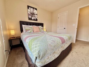 A bedroom with a bed, a nightstand, a wall-mounted lamp, and a door.