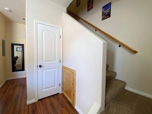 A hallway with a white door, a wooden staircase, and a framed picture on the wall.