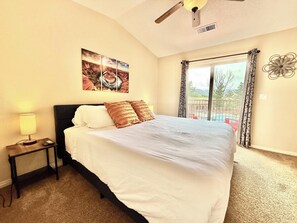 Une chambre d’hôtel avec un lit, une table de chevet, une lampe, un ventilateur de plafond, un tableau et une vue sur l’extérieur.