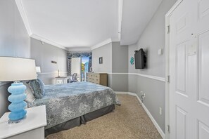 A bedroom with a bed, a nightstand, a lamp, a dresser, a TV, and a door.