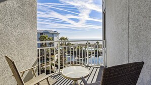 A balcony with wicker chairs and a small table, overlooking a pool and a building with a blue roof. - Luxury Oceanfront Villa w/ Views & Amenities (Hilton Head Island)