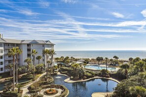 A resort with a pool area, palm trees, and a view of the ocean.