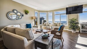 A spacious living room with a large window overlooking the ocean, a comfortable sofa, a coffee table, and a television. - Luxury Oceanfront Villa w/ Views & Amenities (Hilton Head Island)