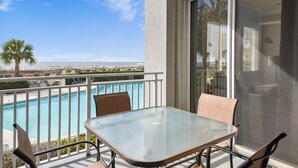 Un balcón con una mesa y sillas de vidrio, con vista a una piscina y una playa.