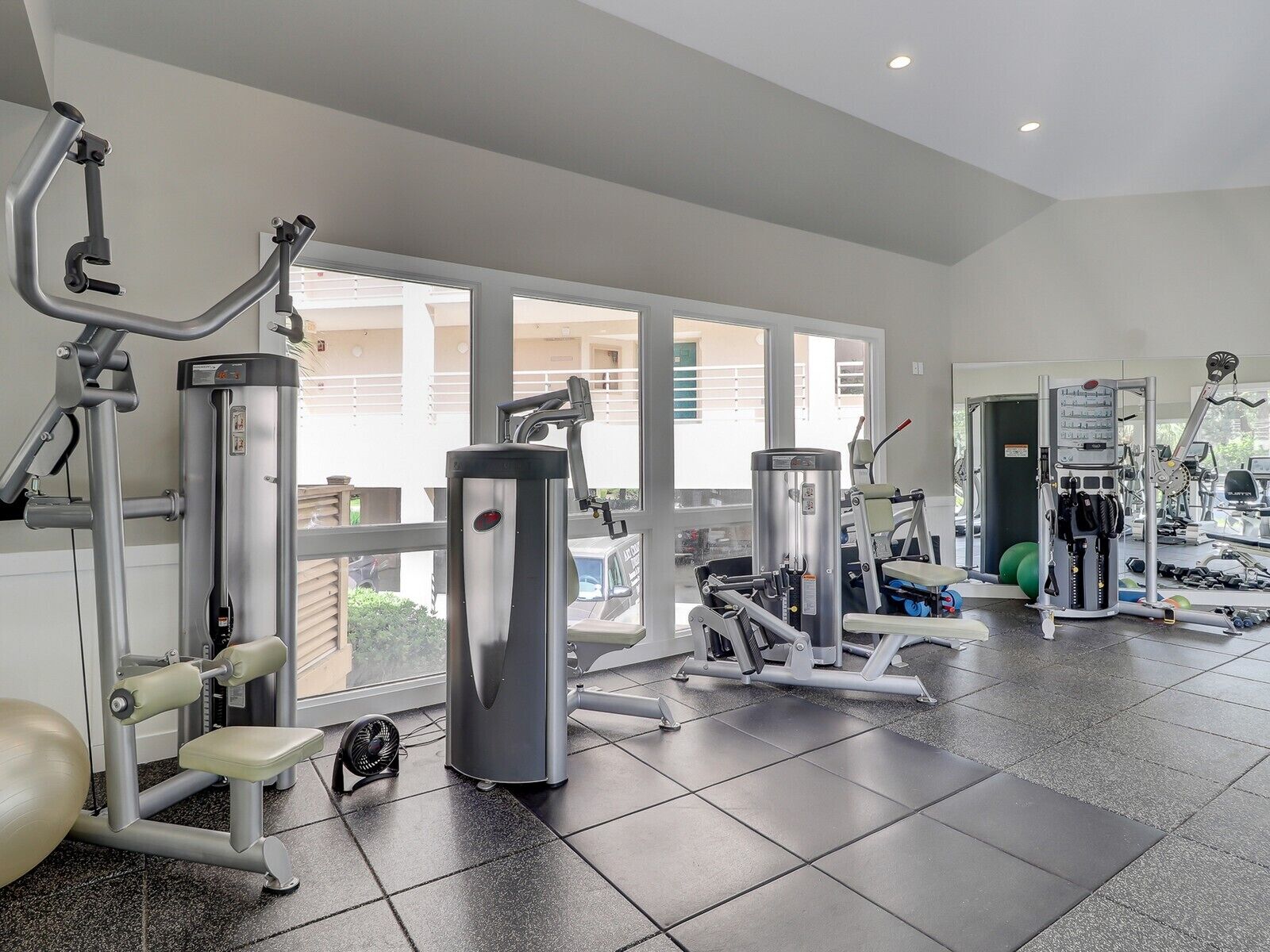 A gym with various exercise machines, a fan, and a large window providing a view of the outside.