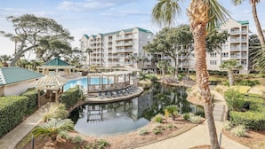 Un resort con piscina, palme e vasca di riflessione circondata da un paesaggio curato.