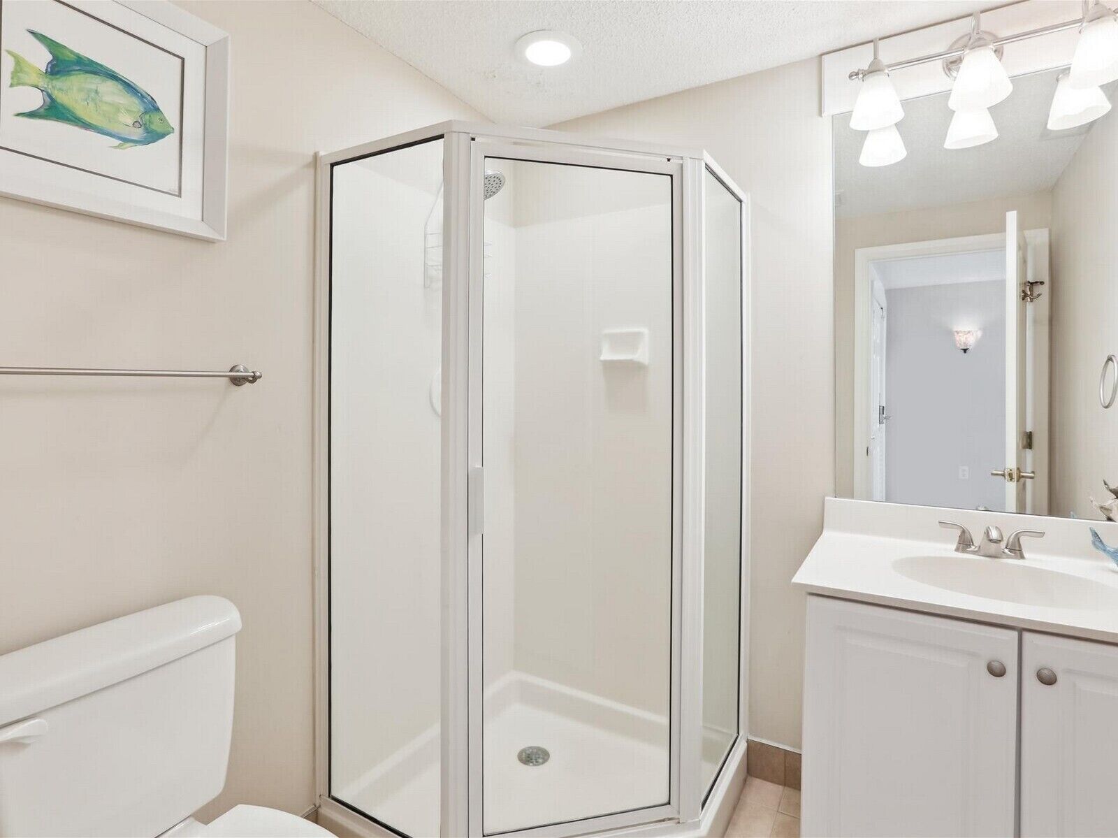 Une salle de bain avec une douche à parois de verre, des toilettes, un lavabo avec un miroir et un tableau représentant des poissons, encadré, accroché au mur.