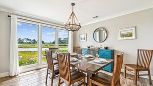 Un coin repas avec une grande fenêtre, des chaises en bois, une table en bois, un lustre, un buffet bleu et un miroir au mur.