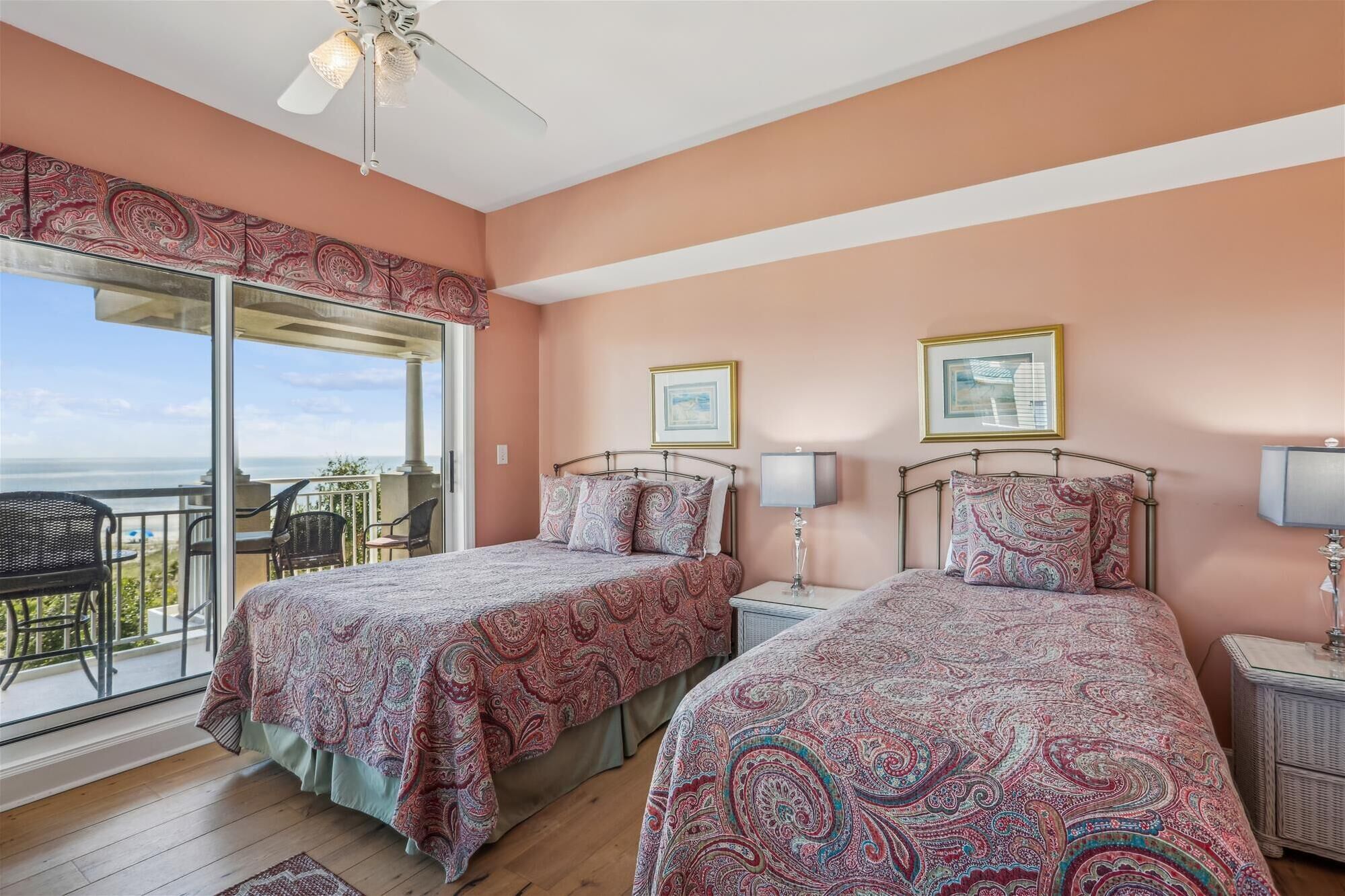 A bedroom with two beds, a balcony with a view, and a ceiling fan.