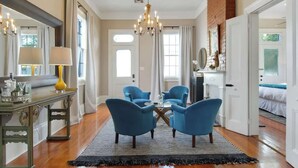 A spacious living room with a chandelier, a coffee table, and blue armchairs.