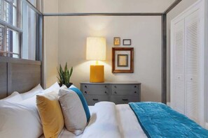 Een netjes opgemaakt slaapkamer met een bed, nachtkastje, lamp en ingelijste foto’s aan de muur.