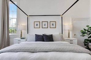 A bedroom with a bed, two bedside tables, a window, and three framed pictures on the wall. - Historic Luxury Retreat (New Orleans)