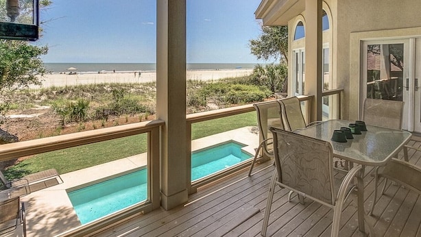 Ein überdachter Außenbereich mit Pool, Terrassenmöbeln und Blick auf den Strand.
