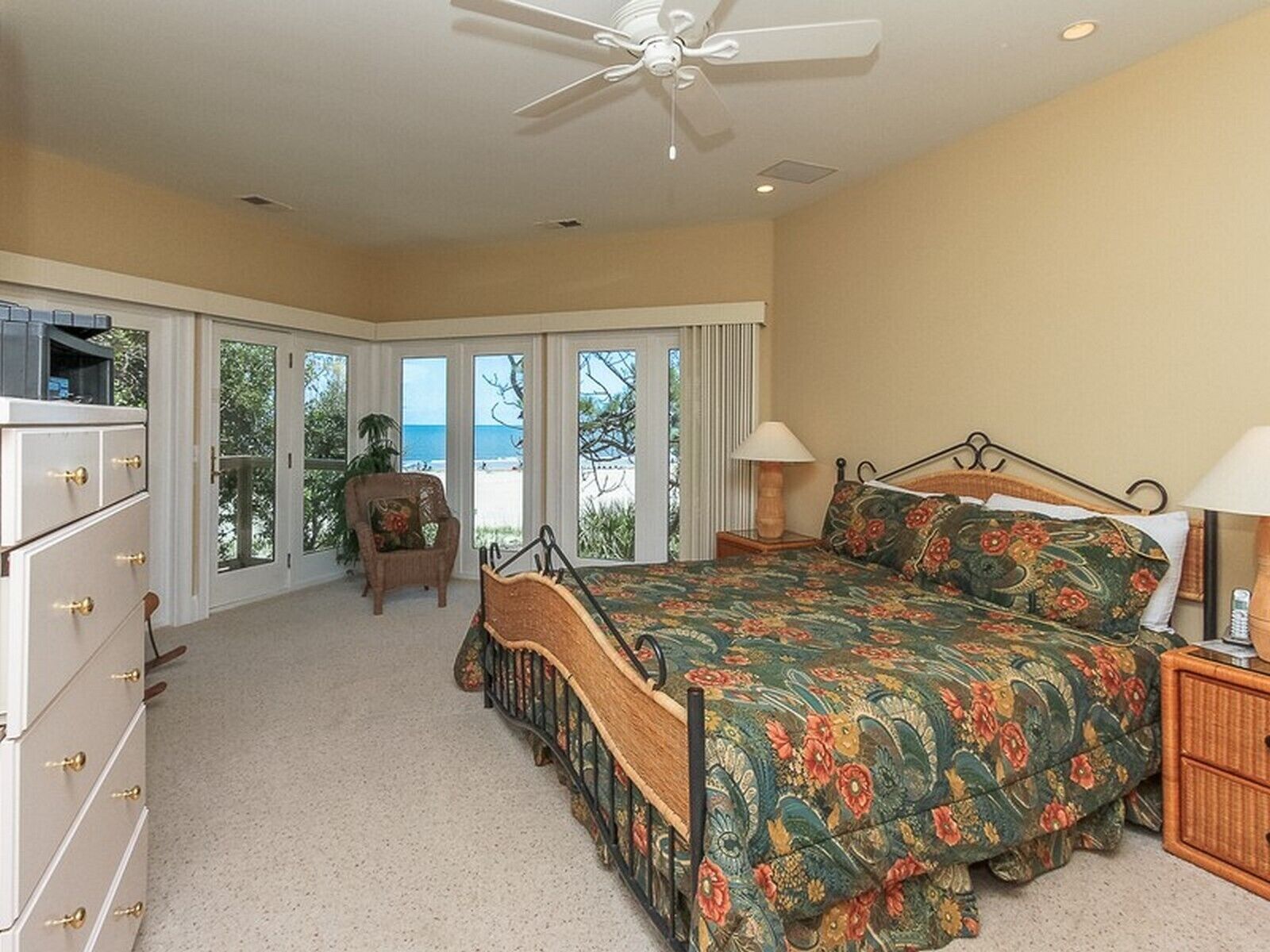 A bedroom with a bed, dresser, chair, and a view of the beach.