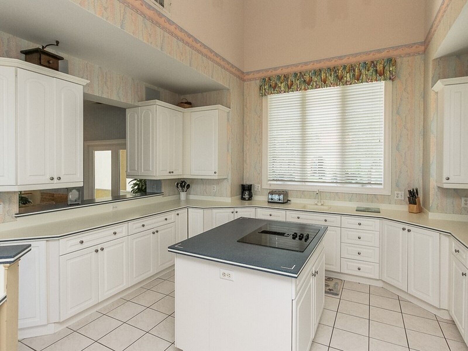 Una cocina amplia con armarios blancos, una isla central con estufa y una ventana con persianas.