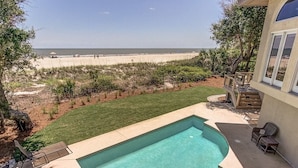 Ein Pool mit Blick auf den Strand, umgeben von einer gepflegten Rasenfläche und einer Terrasse mit Sitzgelegenheiten.