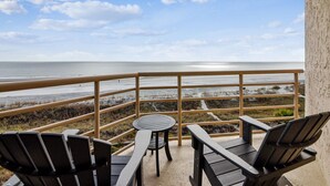 Ein Balkon mit Blick auf den Strand, zwei Stühle und ein kleiner Tisch.