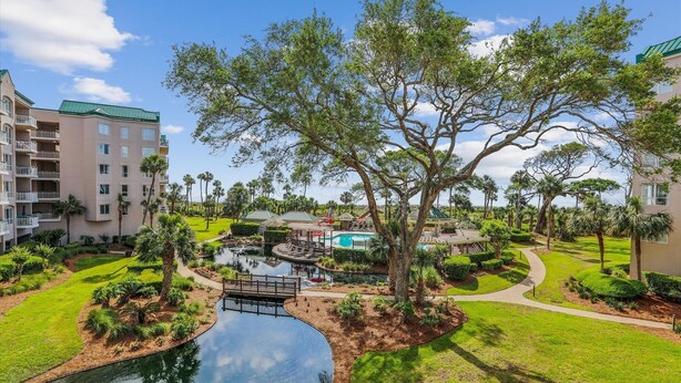 Un resort con piscina, un puente y un árbol grande en el centro.