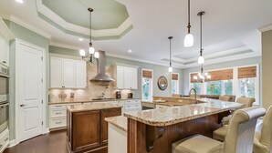 Una cocina amplia con una isla grande, armarios blancos e iluminación colgante.