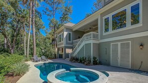Una propiedad residencial con piscina, jacuzzi y un área exterior cubierta con una escalera que lleva a un balcón.