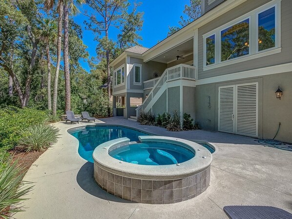 A residential property with a swimming pool, a hot tub, and a covered outdoor area with a staircase leading to a balcony.