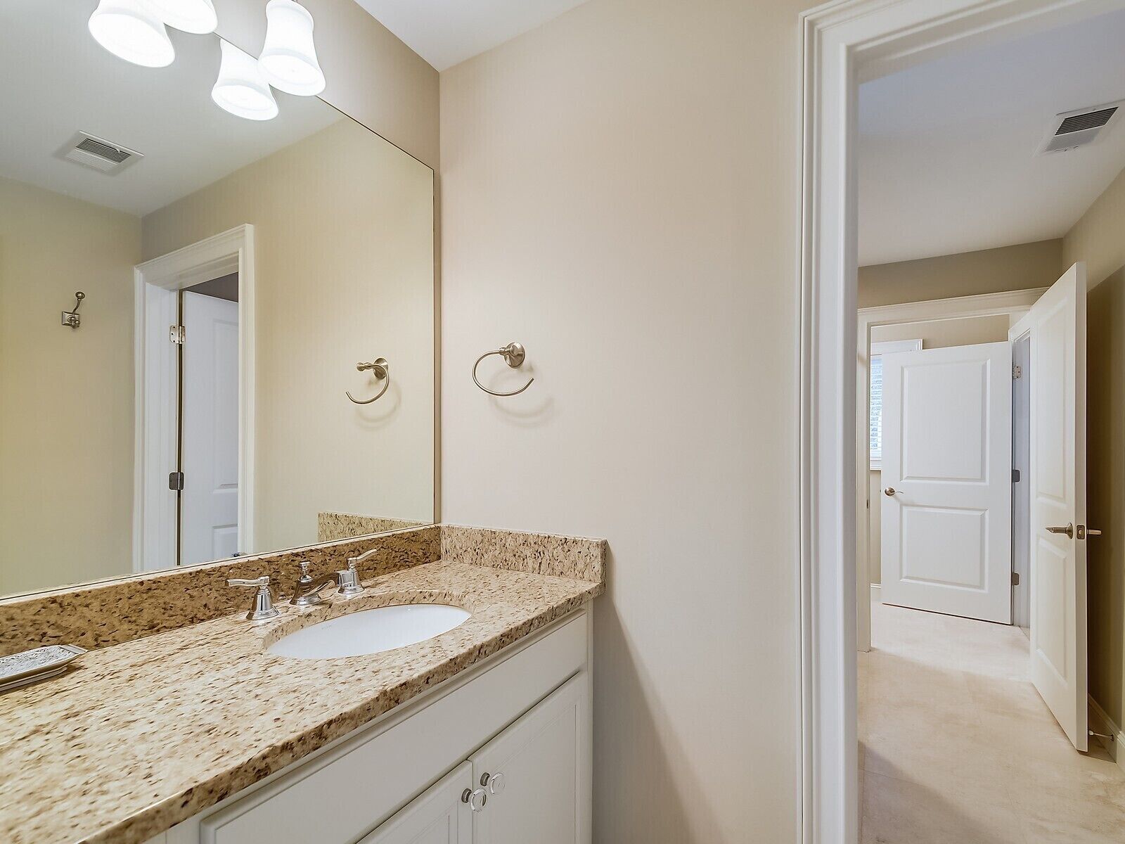 A bathroom with a granite countertop, two sinks, a large mirror, and a door leading to another room.