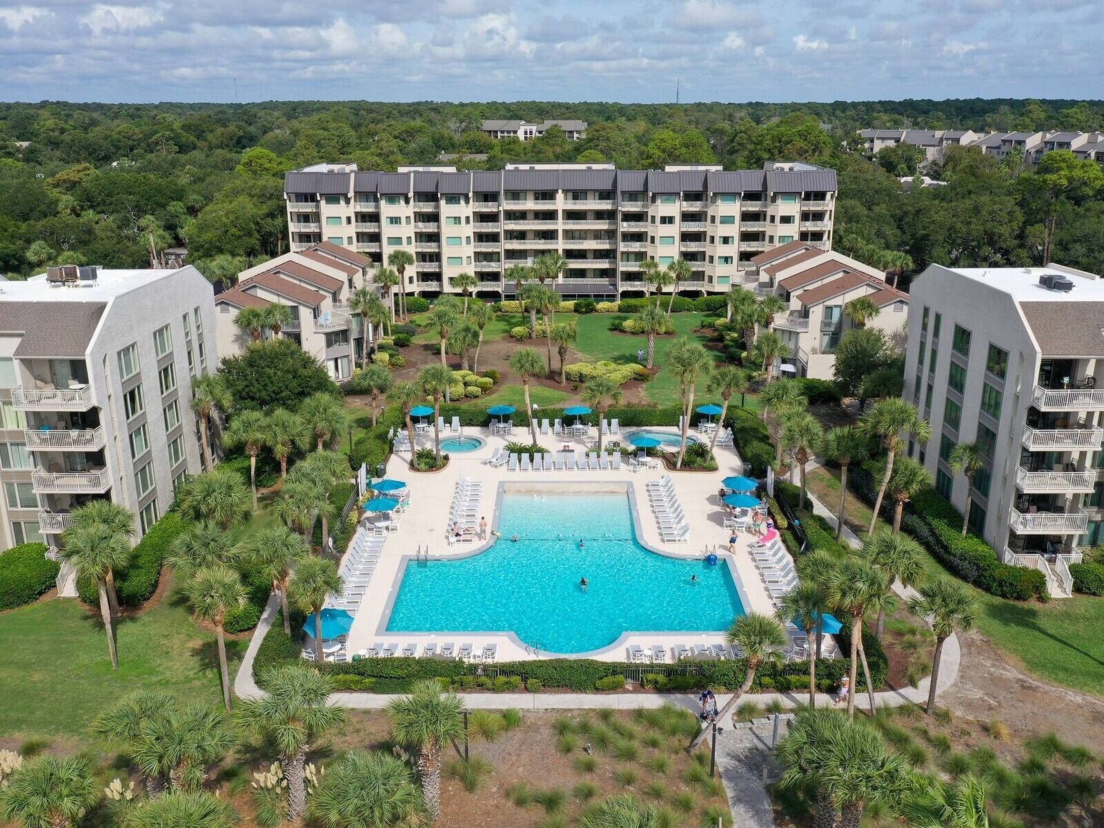Un hotel con piscina centrale circondata da poltrone a sdraio e ombrelloni, con diversi piani e un giardino curato.
