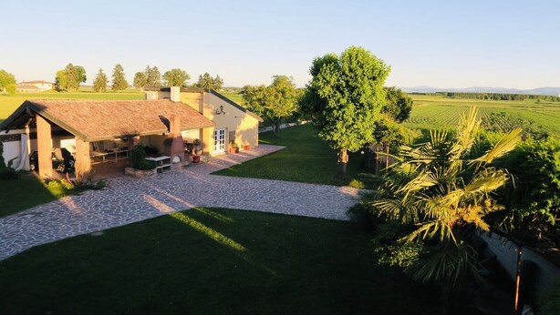 A rustic house with a stone patio, a covered outdoor seating area, and a view of a lush green field. - The house in the fields_Dépendance (Lombardia)