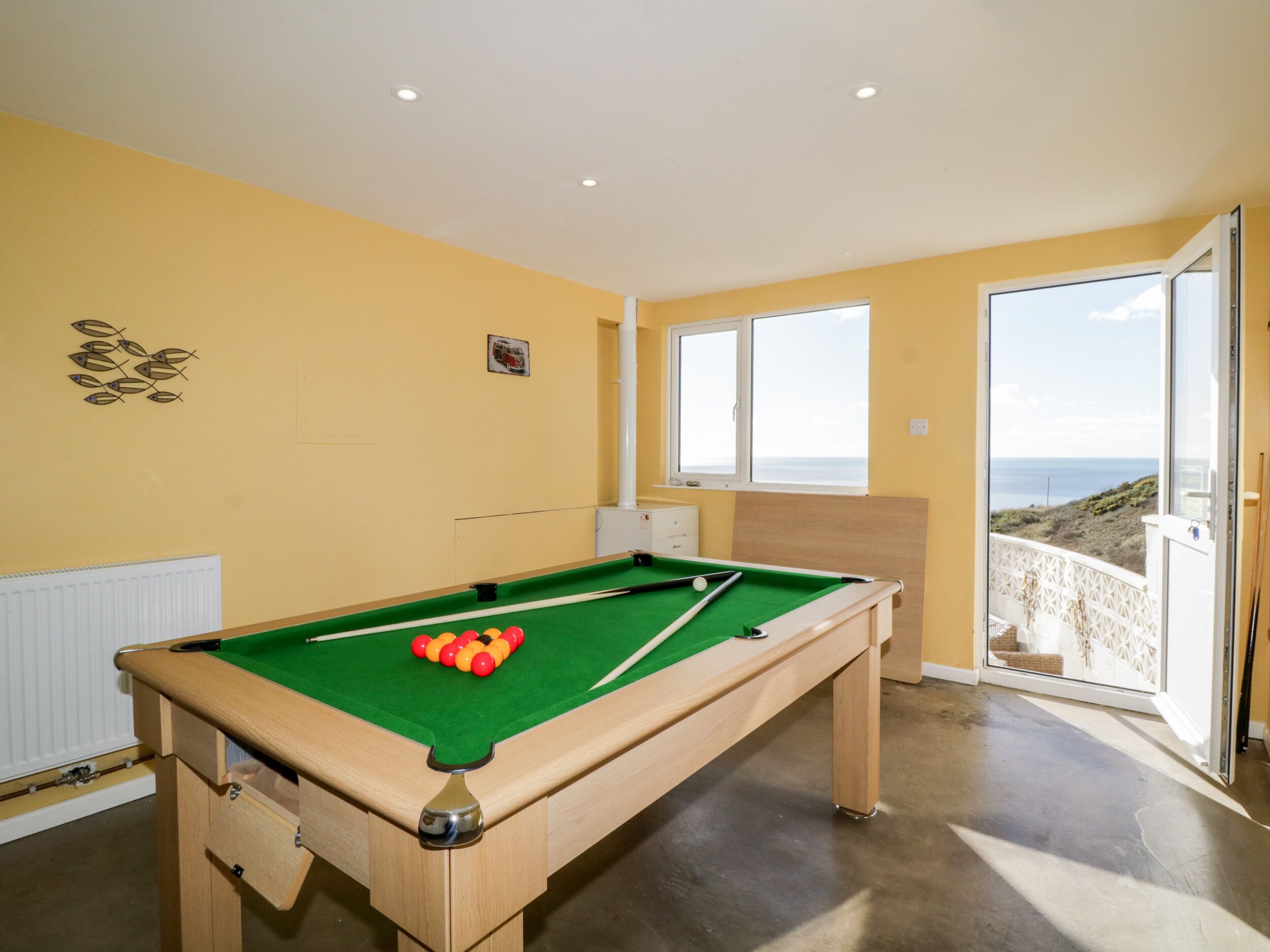 A pool table with balls, a radiator, and a window with a view of the sea.